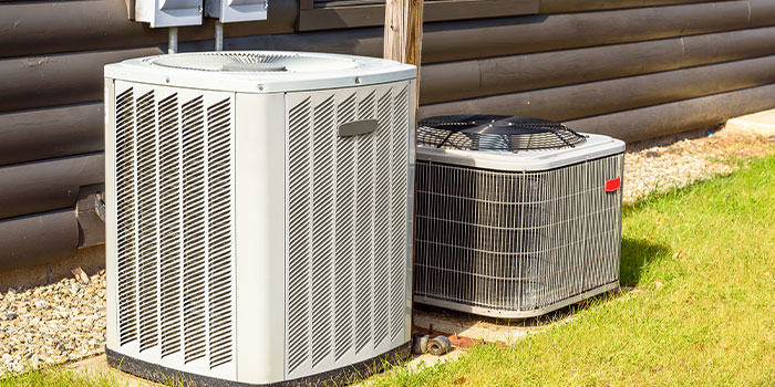 Two outdoor AC units installed beside a building on grass.
