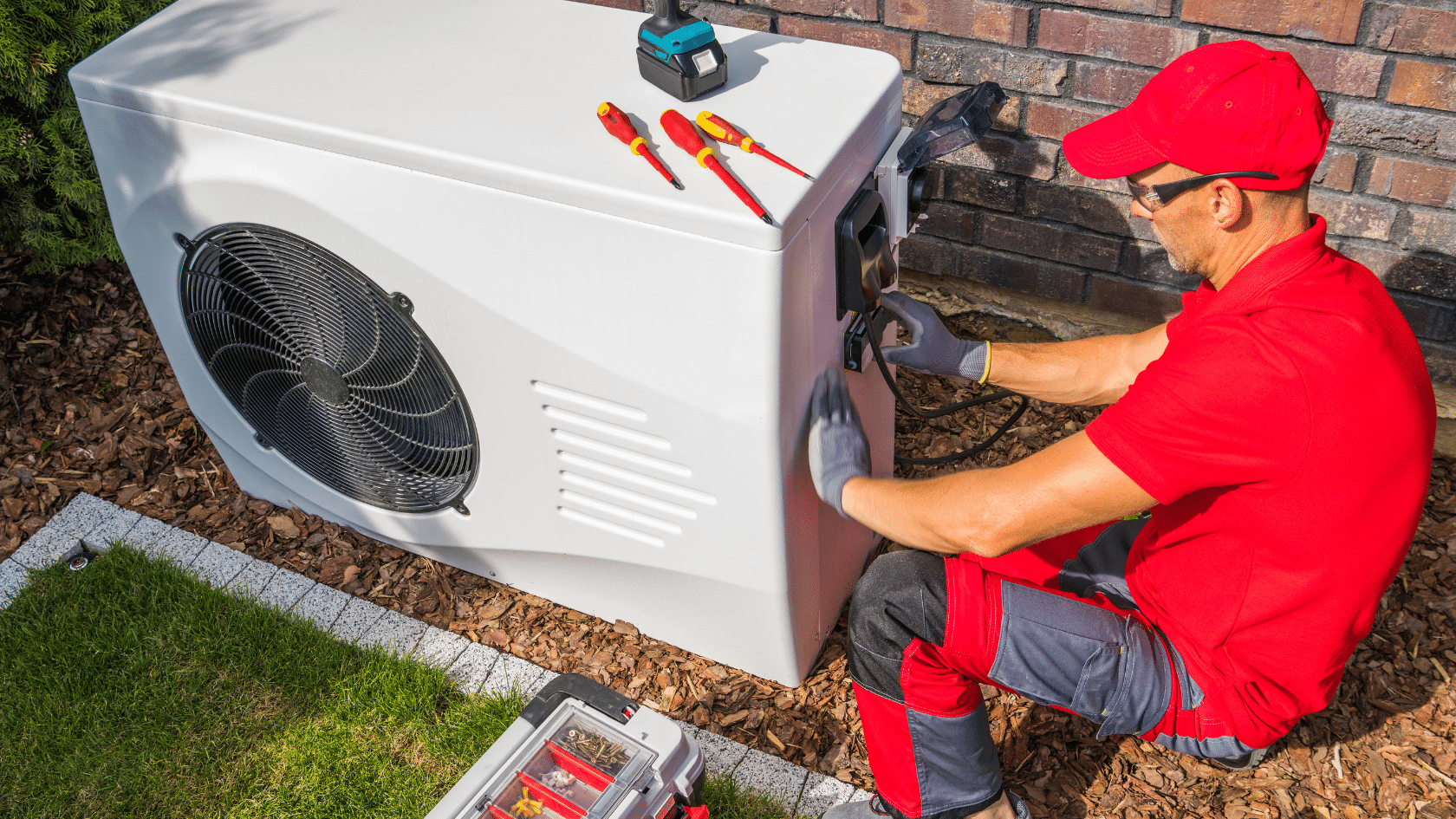 Technician in red uniform working on outdoor heat pump installation.