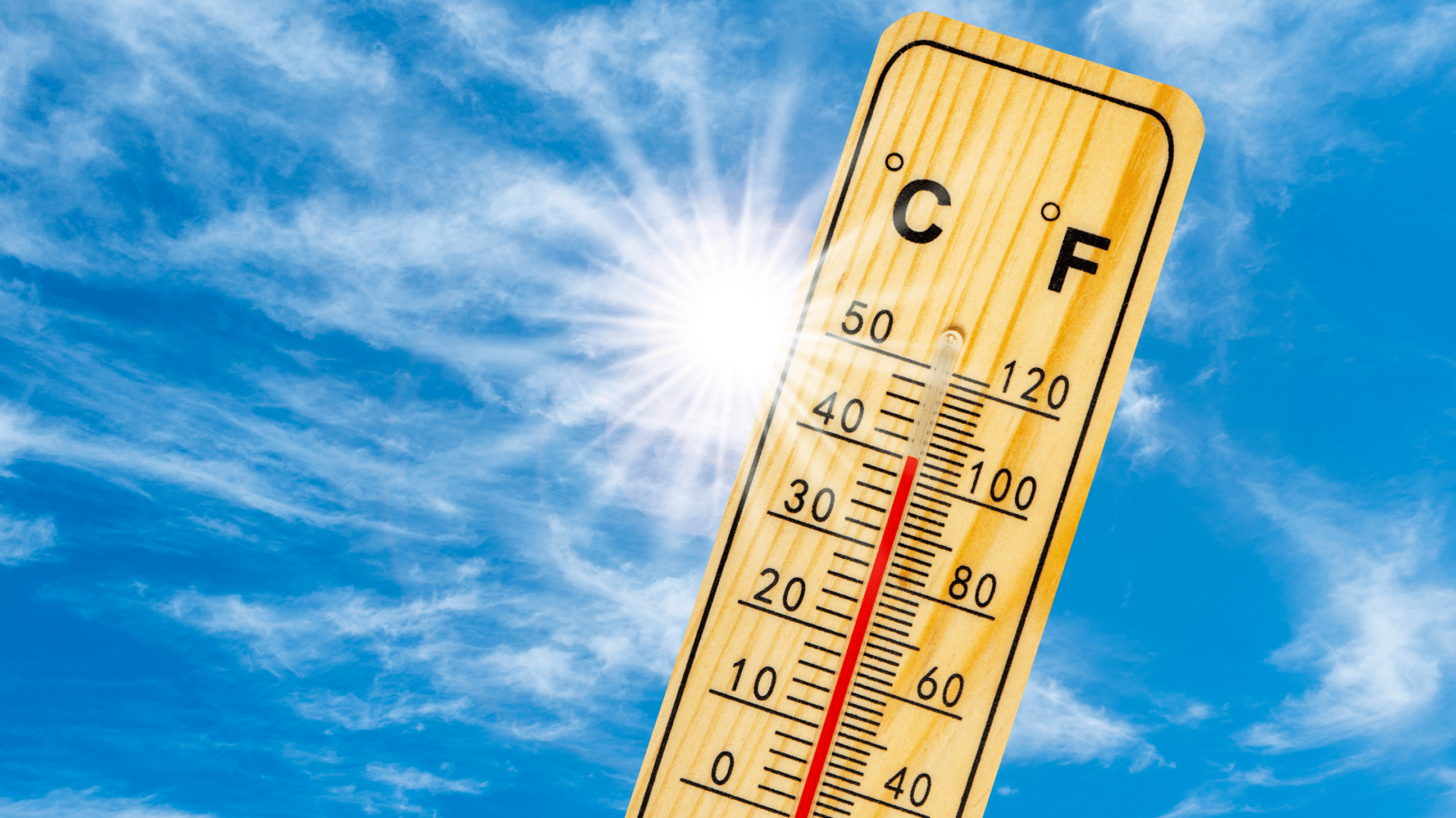 Thermometer reading high temperature under bright sun in blue sky.