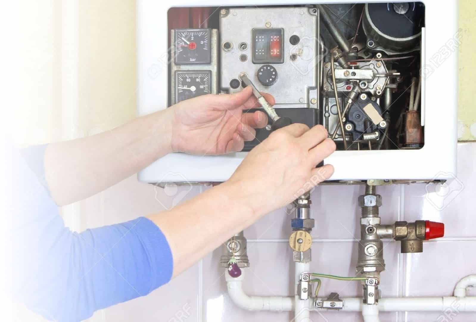 Person adjusting controls on a gas boiler system.