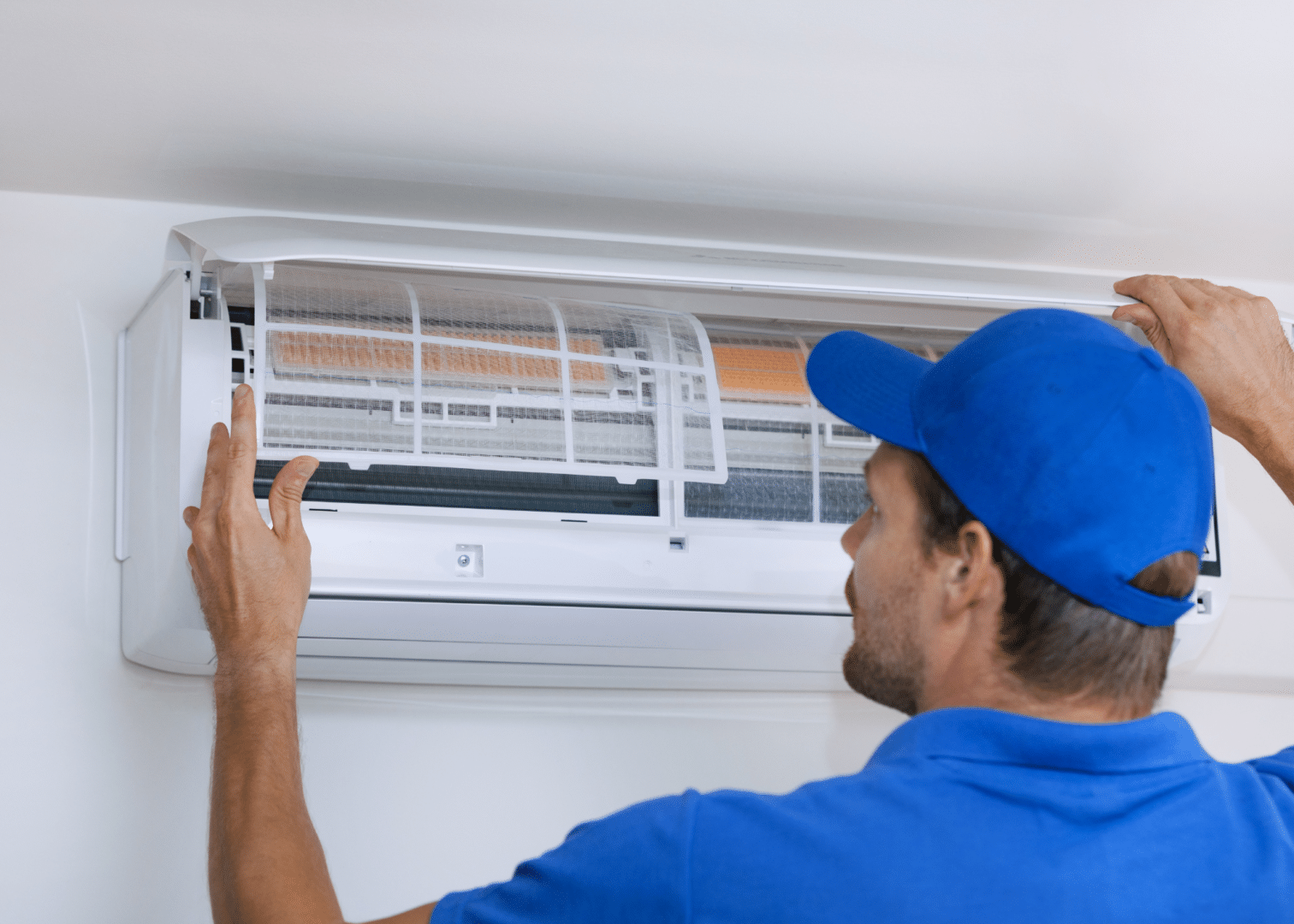 A technician in a blue cap inspects and adjusts an air conditioning unit.