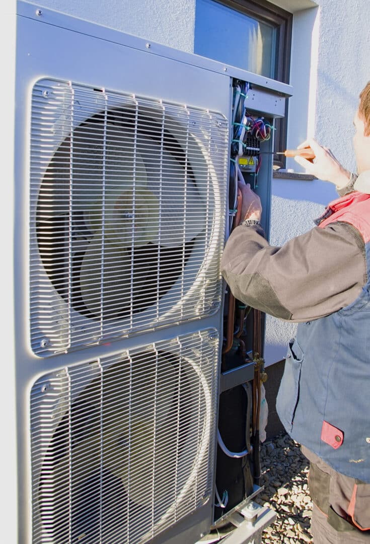 A person repairing an outdoor air conditioning unit with tools.