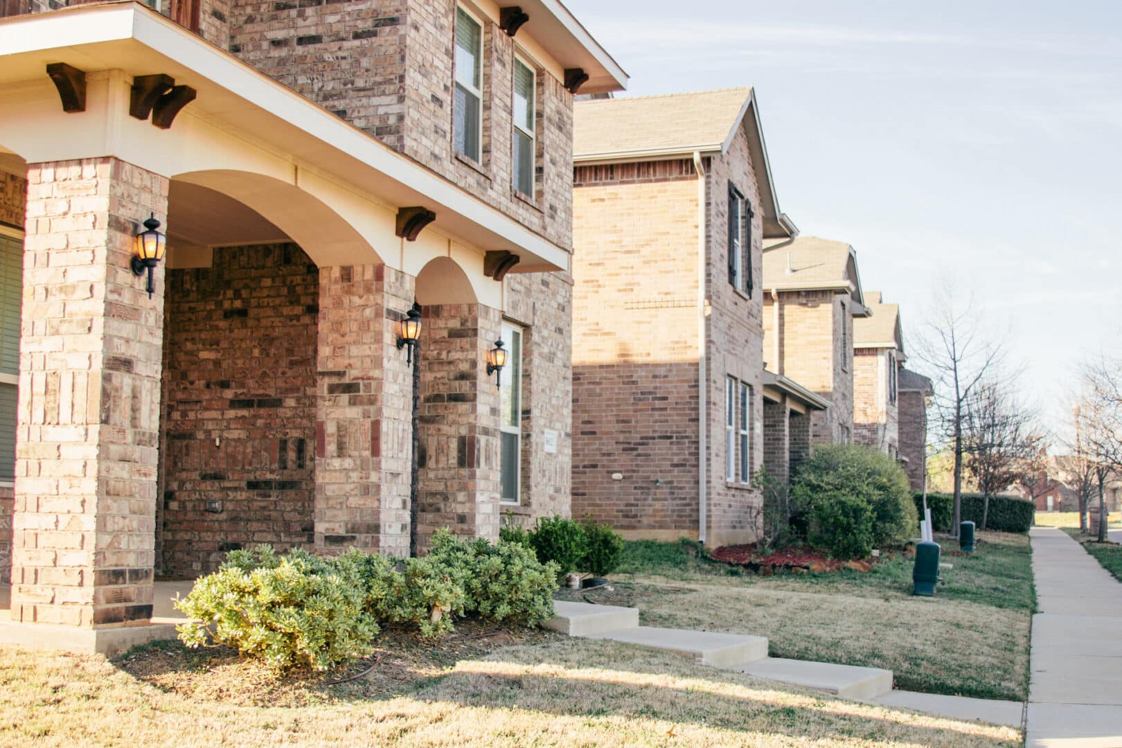 Row of brick houses with trimmed bushes and pathway.