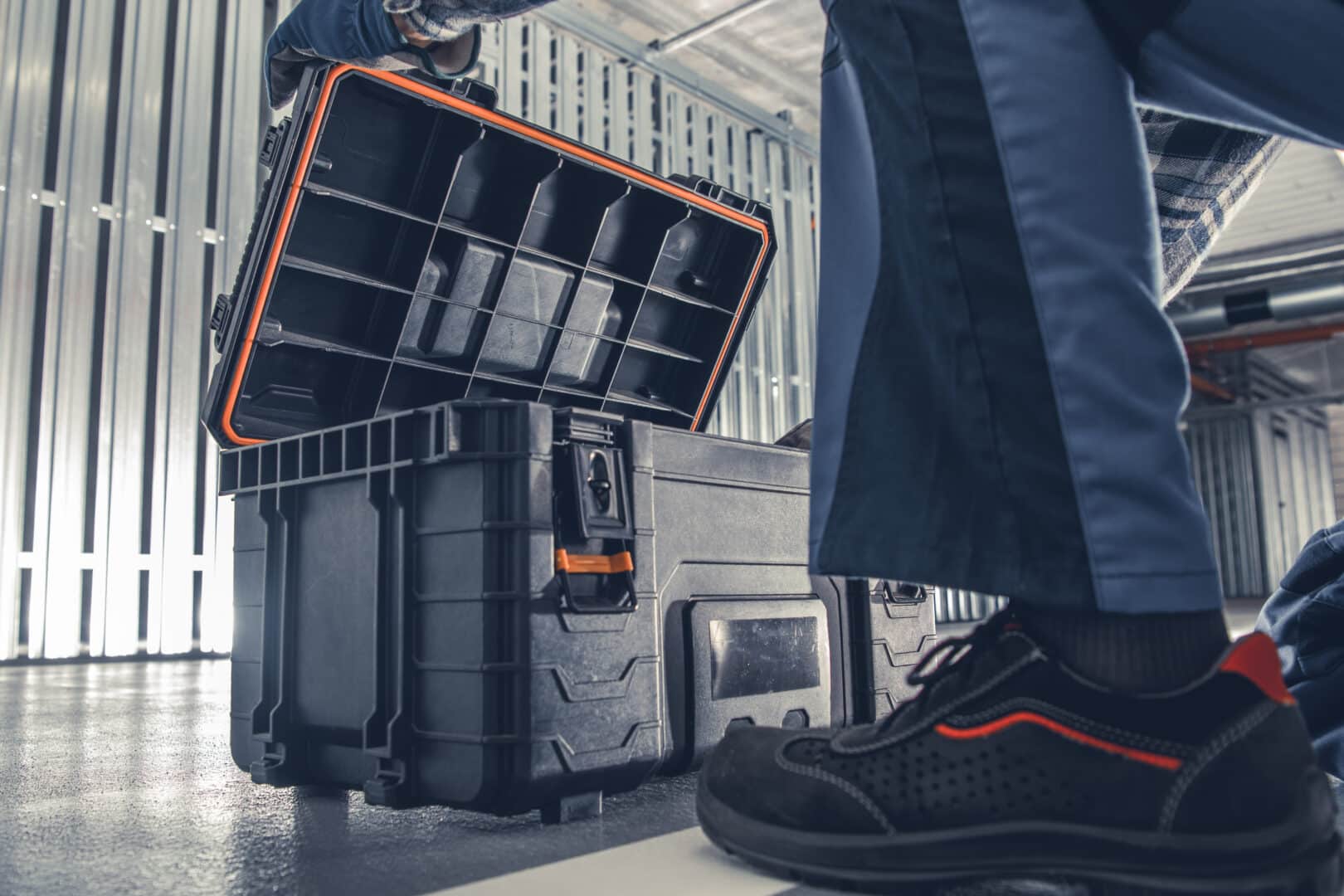 Person opening a toolbox in an industrial setting with metal walls.