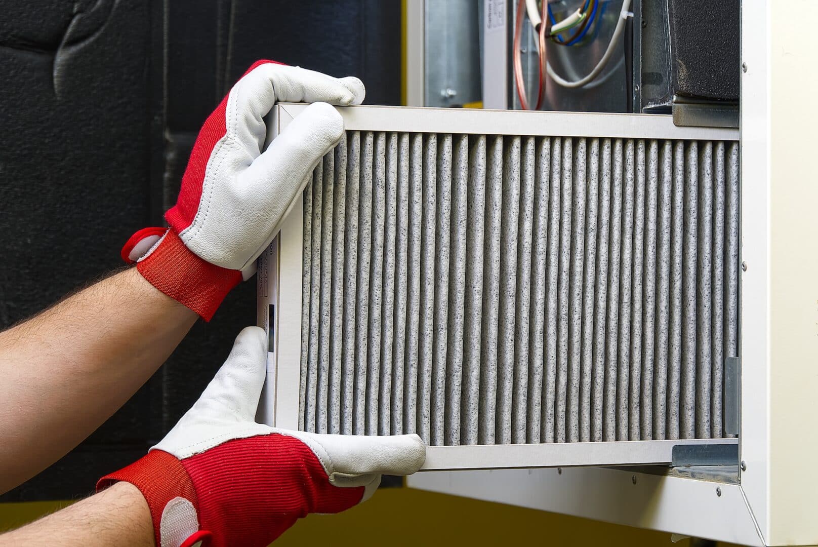 Hands in gloves changing an air filter in a HVAC system.