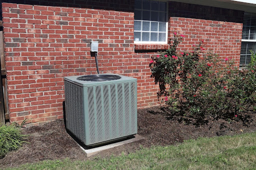 Outdoor air conditioning unit beside a red brick wall and garden roses.
